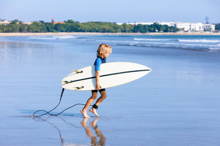 Happy surf boy - young surfer run to ride on surfboard with fun on sea waves. Active family lifestyle, kids outdoor water sport lessons, swimming activity in surfing camp. Summer vacation with child